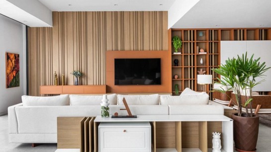 Dois ambientes integrados compõem esta sala projetada pela Criare Recife; o espaço de TV conta com um painel ripado no padrão amadeirado e tem a frente um painel no padrão Sienna, que é utilizado também na estante do espaço de estar. Foto: Divulgação.